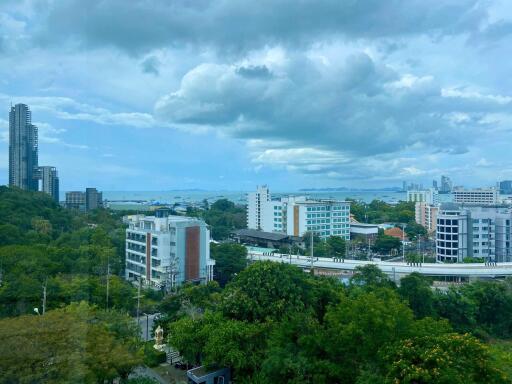 Scenic view of a cityscape from a high-rise building showing nearby apartments, lush greenery, and distant ocean views under a cloudy sky