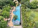 Aerial view of a tropical resort-style pool with waterslide surrounded by lush greenery