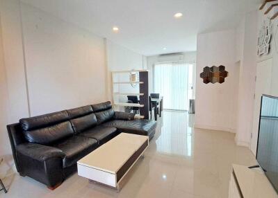 Spacious modern living room with glossy tiled flooring, black leather couch and direct access to kitchen