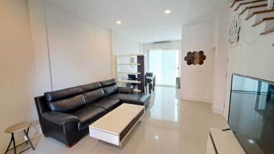 Spacious modern living room with glossy tiled flooring, black leather couch and direct access to kitchen