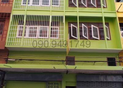 Bright green multi-story building facade with balconies and commercial space on ground floor