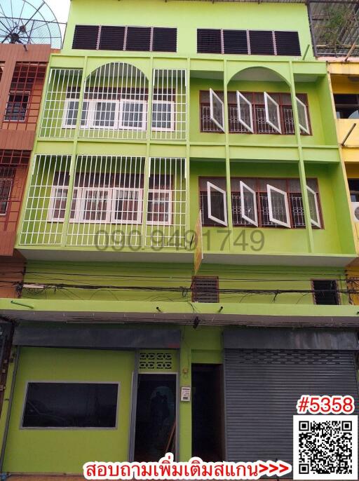 Bright green multi-story building facade with balconies and commercial space on ground floor