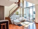 Modern living room interior with large windows, wooden flooring, and a staircase