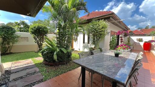 Spacious tiled patio with outdoor dining table, well-maintained garden and tropical plants, in a sunny backyard of a residential home