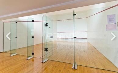 Indoor home gym with a squash court featuring hardwood floors and glass partitions