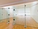 Indoor home gym with a squash court featuring hardwood floors and glass partitions