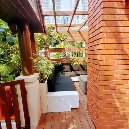 Cozy balcony with wooden flooring and modern brick walls surrounded by green plants under a pergola