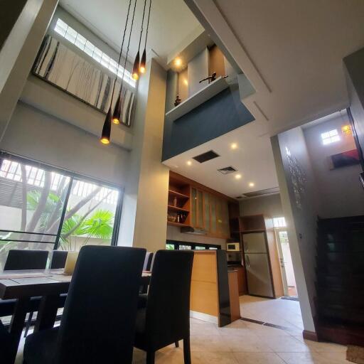 High ceiling dining area with modern lighting and adjacent kitchen