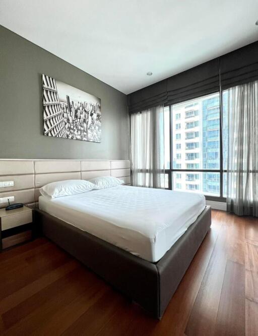 Modern bedroom with queen-sized bed, hardwood floors, and large window with city view