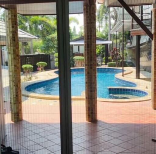 View of a swimming pool through glass doors from a tiled room, suggesting a backyard or patio area