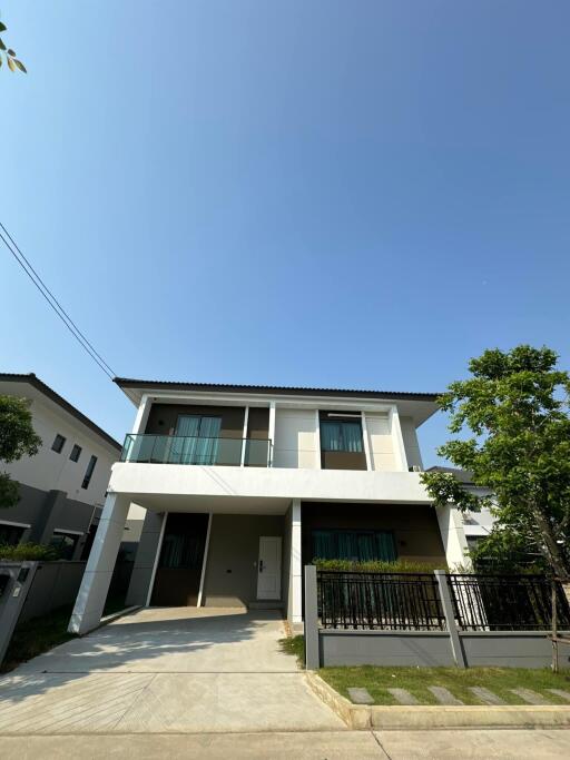 Modern two-story house with balcony and front yard under a clear sky