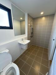 Modern bathroom with tiled walls and flooring, featuring a toilet, sink, mirror, and shower area