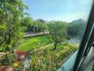 Expansive view from a window overlooking a lush green garden with pathway and surrounding houses