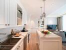 Modern kitchen with integrated living space featuring wooden floors, white cabinetry, and stainless steel appliances