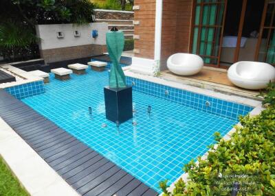 Modern home exterior with a sparkling blue pool surrounded by a wooden deck and comfortable poolside furniture