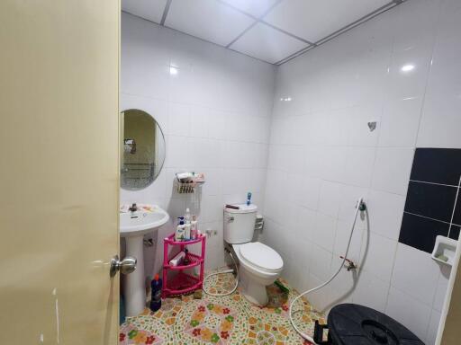 Compact white-tiled bathroom with essential fixtures and colorful floor