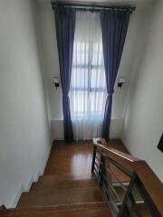 Staircase landing with wooden floor and window dressed with blue curtains