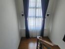 Staircase landing with wooden floor and window dressed with blue curtains