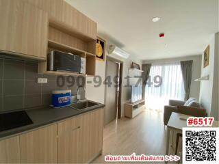 Modern apartment kitchen with living space, featuring wooden cabinetry and natural light