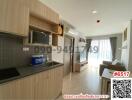 Modern apartment kitchen with living space, featuring wooden cabinetry and natural light