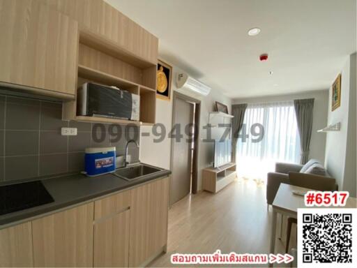 Modern apartment kitchen with living space, featuring wooden cabinetry and natural light