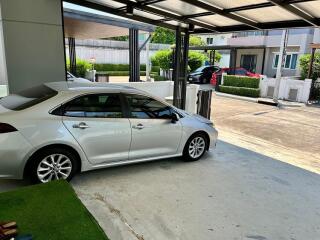 Car parked under a shaded carport with residential buildings in the background