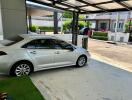 Car parked under a shaded carport with residential buildings in the background