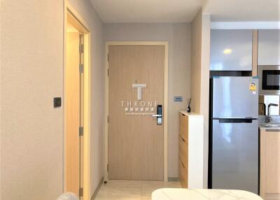 Modern apartment entryway with light wood door, adjacent kitchen and refrigerator