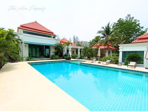 Luxurious villa with a large swimming pool surrounded by palm trees and well-maintained garden