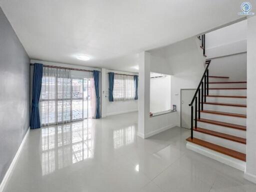 Spacious and bright living room with glossy tiled floor and staircase to upper level