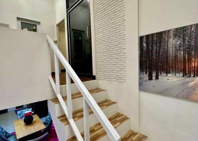 Interior view of a stairway leading to an upper level with a wooden banister and a photograph of a winter forest scene on the wall