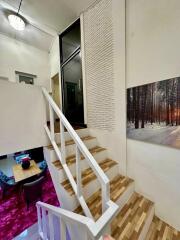 Interior view of a stairway leading to an upper level with a wooden banister and a photograph of a winter forest scene on the wall