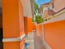 Narrow outdoor passage of a residential building with bright orange walls and a clear blue sky