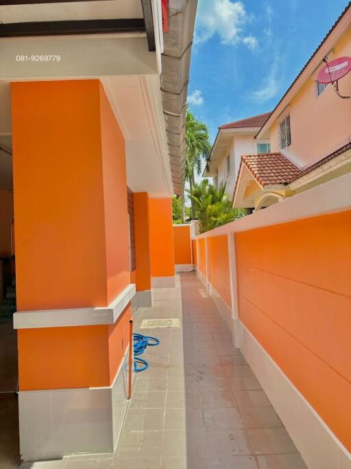 Narrow outdoor passage of a residential building with bright orange walls and a clear blue sky