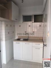 Compact white tiled kitchen with upper and lower cabinets and a sink