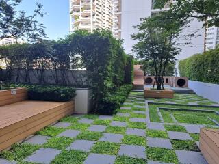 Modern outdoor common space with green landscaping, benches, and walking paths between apartment buildings