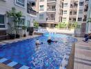 Residents enjoying a sunny day at the communal swimming pool surrounded by apartment buildings