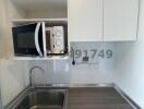 Compact modern kitchen with stainless steel sink, microwave, and white cabinets