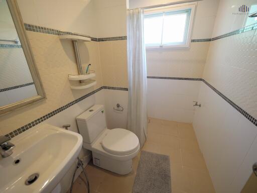 Compact bathroom with tiled walls, shower curtain, and natural light