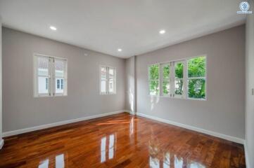 Spacious bedroom with natural lighting, polished hardwood floors, and a view of greenery through the windows