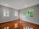 Spacious bedroom with natural lighting, polished hardwood floors, and a view of greenery through the windows