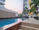 Communal swimming pool with palm trees and apartment buildings in the background at dusk