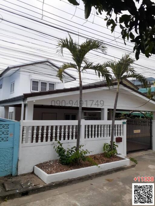 White two-story house with fenced front garden and palm trees