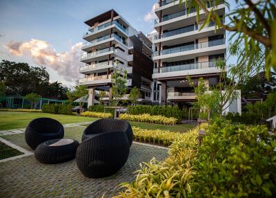 Modern multi-story residential building with lush green lawn and stylish outdoor seating