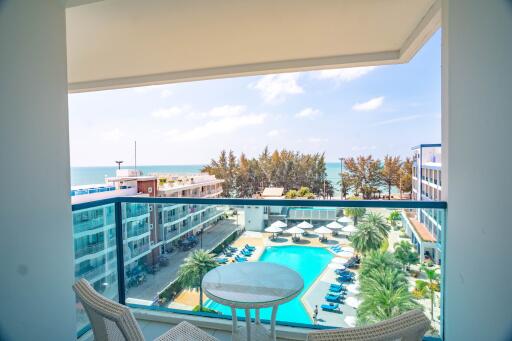 Bright balcony with sea view and outdoor furniture overlooking a resort pool area