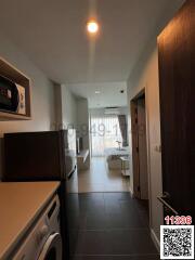 Modern apartment interior view showing a compact kitchen leading into a bright living space