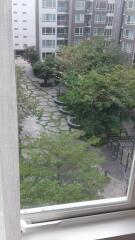 View from a window showing a well-maintained communal garden with walking paths in an apartment complex