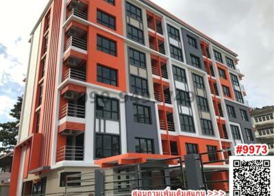 Modern multi-story residential building with orange and grey facade under a cloudy sky