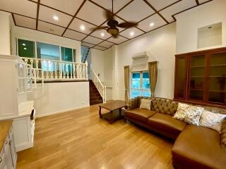 Spacious living room with high ceiling, wooden floors, and staircase