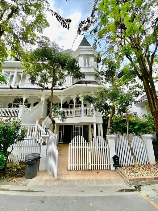 Elegant Victorian-style house with a white fence surrounded by greenery